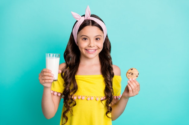 Retrato de niña positiva mantenga vaso de leche sabrosas galletas de chocolate dulce