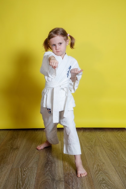 Retrato de niña practicando karate contra la superficie amarilla