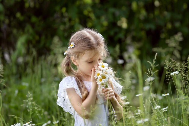 Retrato de niña preescolar con flores de margarita en largos cabellos rubios Niños al aire libre con flores de margaritas Concepto de verano