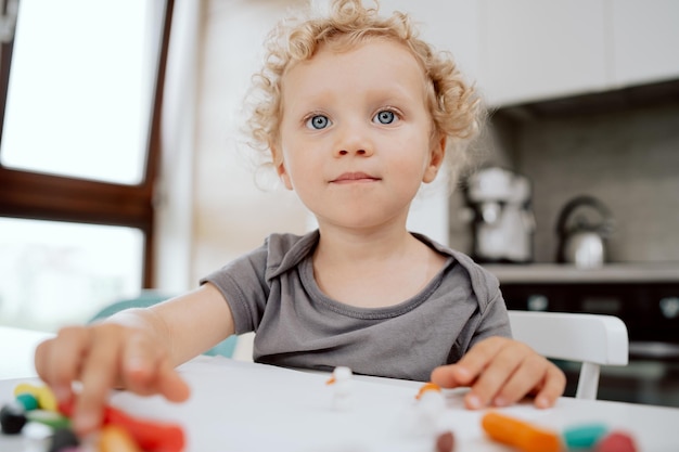 Retrato de una niña preescolar sonriente sentada en la mesa de su cocina jugando con plastilina el amor lindo