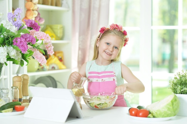 Retrato de niña preparando ensalada en la mesa de la cocina