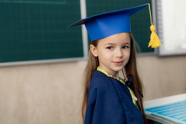 retrato de una niña de primer grado en un sombrero festivo posando para una foto en un escritorio en un aula