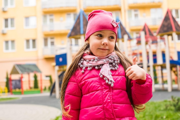 Retrato de niña con el pulgar hacia arriba en el patio de recreo al aire libre A la niña activa le encanta pasar tiempo al aire libre en cualquier época del año