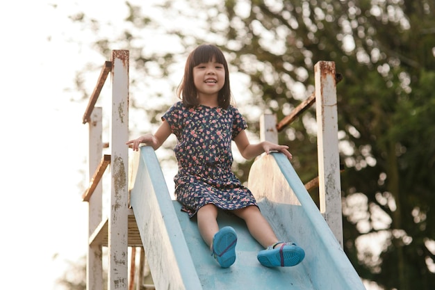 Foto retrato de una niña que se desliza por un tobogán en un parque