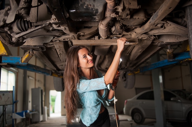 Retrato de niña que examina el coche levantado en el taller de reparación de automóviles