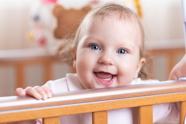 Retrato de una niña que se ríe y se para en una cuna en la habitación