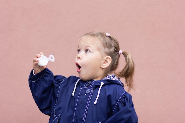 Retrato de la niña que sopla pompas de jabón en el fondo rosa