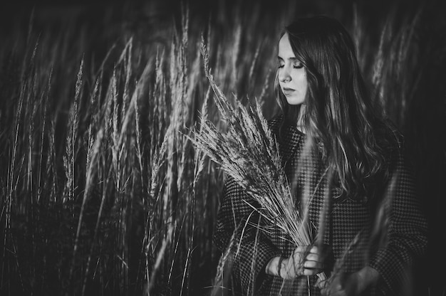 Retrato de niña con un ramo de hierba seca en otoño en una hierba alta y alta