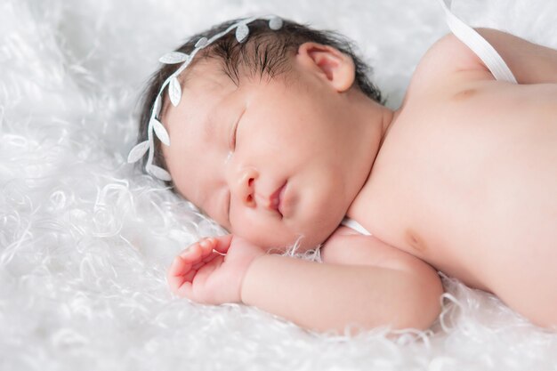 Retrato de una niña recién nacida durmiendo de un mes. Lleva una diadema de corona y duerme sobre una manta blanca. Concepto retrato estudio moda recién nacido.