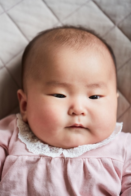 Retrato de niña recién nacida linda asiática en hermoso vestido rosa acostado en la cama