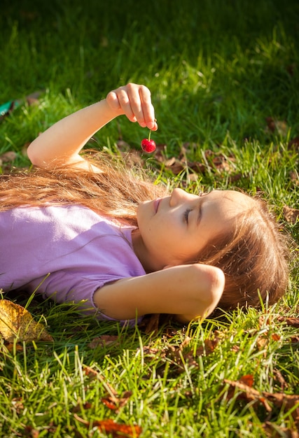 Retrato de niña recostada sobre la hierba y mirando rojo cereza