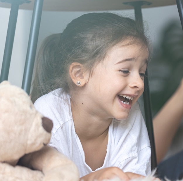 Retrato de una niña riendo cerca de un oso de peluche en casa.