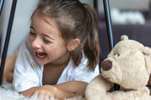 Retrato de una niña riendo cerca de un oso de peluche en casa.