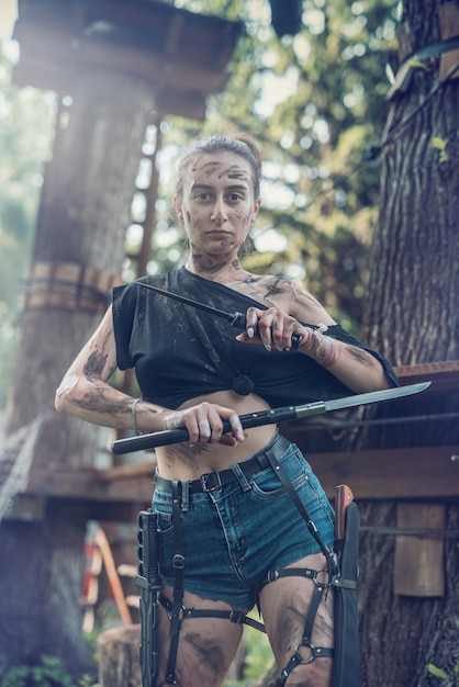Foto retrato de niña con ropa rasgada sosteniendo un cuchillo y posando en el bosque