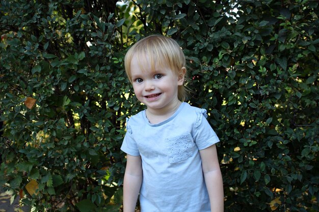 Foto retrato de una niña rubia de 2 años sobre un fondo de hojas niño pequeño caucásico con ojos grandes parece