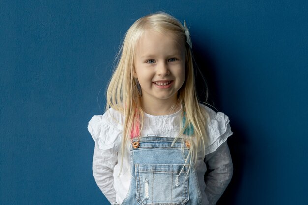 Retrato de niña rubia feliz de 4 años al aire libre contra árboles verdes y cielo azul