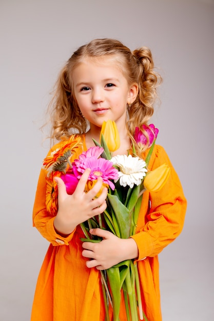 Retrato de una niña rubia con un ramo de flores de primavera en una pared de luz
