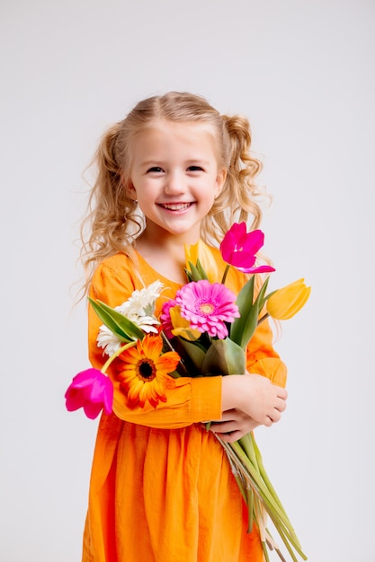 Retrato de una niña rubia con un ramo de flores de primavera en una pared de luz