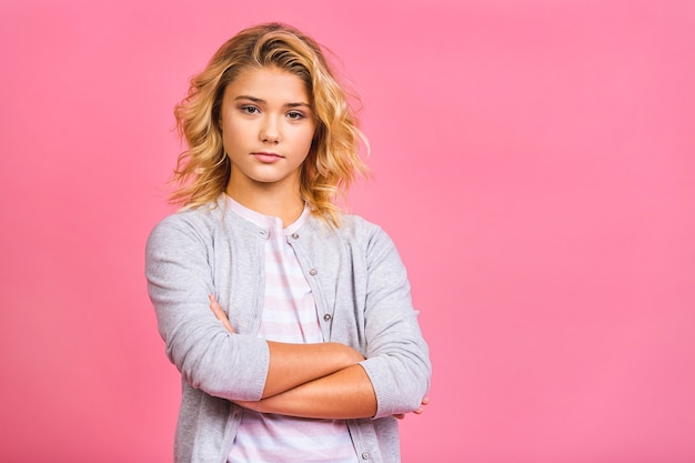 Retrato de una niña rubia seria aislada sobre fondo rosa.