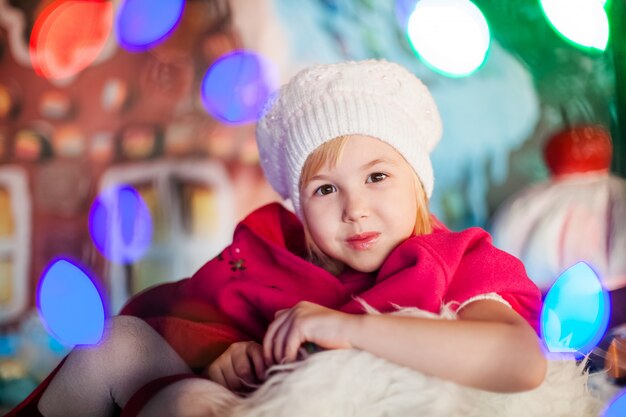 Retrato de niña rubia sonriente con boina blanca, botas rojas, capa rosa