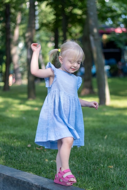 Retrato de niña rubia en vestido azul en el parque Niño de tres años en vestido de verano con dos colas en el fondo de los árboles