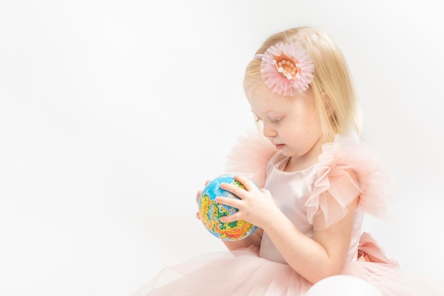 Retrato niña rubia en vestido rosa aislado sobre fondo blancoEl niño mira con entusiasmo pequeño globo en las manos