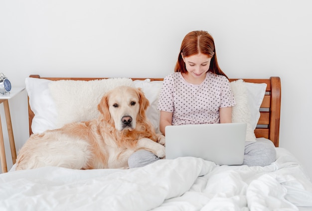 Retrato de niña sentada en la cama con perro y mirando la pantalla del portátil