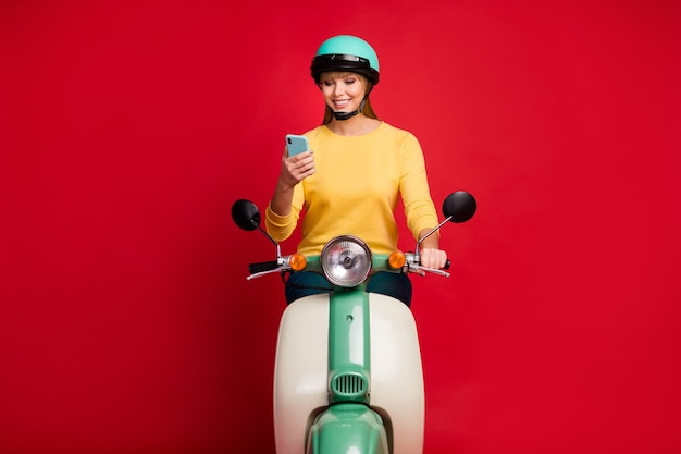 Retrato de niña sentada en el ciclomotor con celular leer sms sobre fondo rojo.