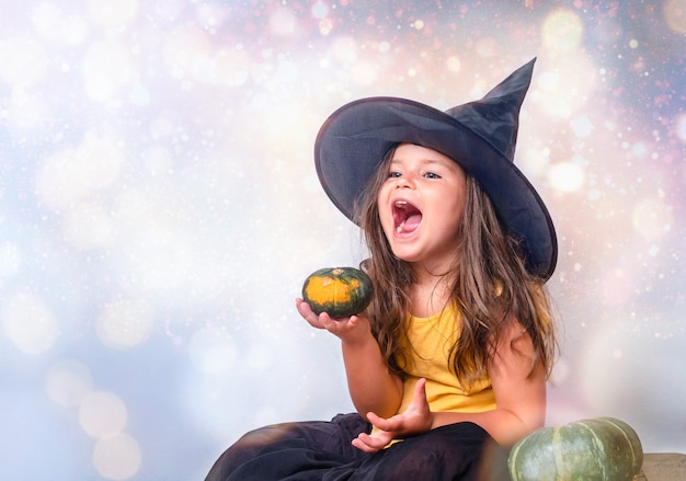 Retrato de la niña con sombrero de bruja con calabaza en el fondo mágico