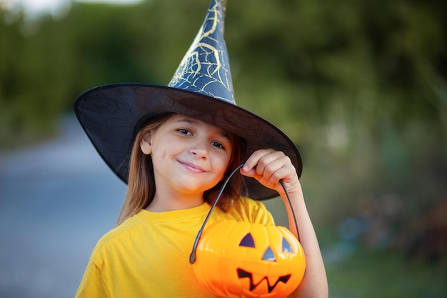 Retrato de una niña en un sombrero de bruja con un tazón de dulces en forma de calabaza en sus manos