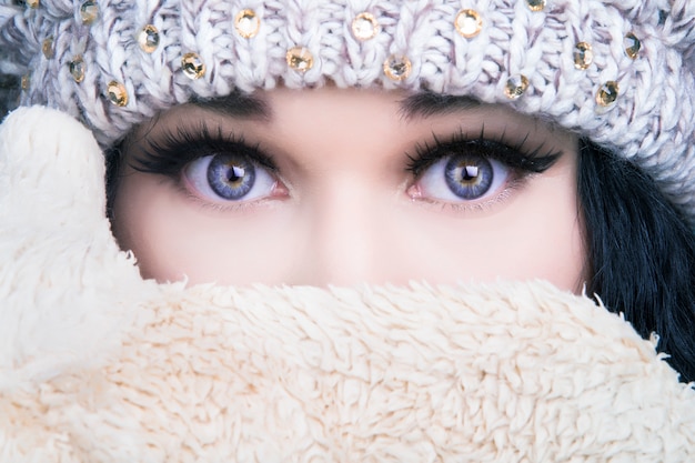 Retrato de una niña con un sombrero y guantes que cubren su rostro, concepto de invierno frío