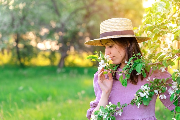 Retrato de una niña con un sombrero de paja disfrutando del aroma de un manzano floreciente en el jardín al atardecer