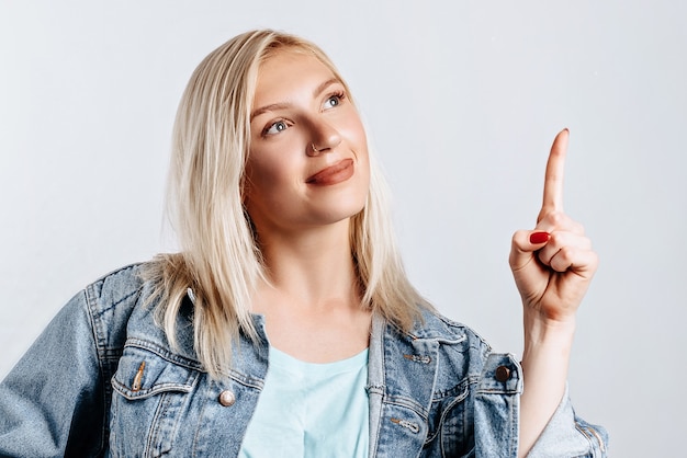 Retrato de una niña sonriente apuntando con el dedo hacia arriba en copyspace aislado sobre un fondo blanco. Una mujer señala una idea, un lugar para publicidad. Rubia positiva.