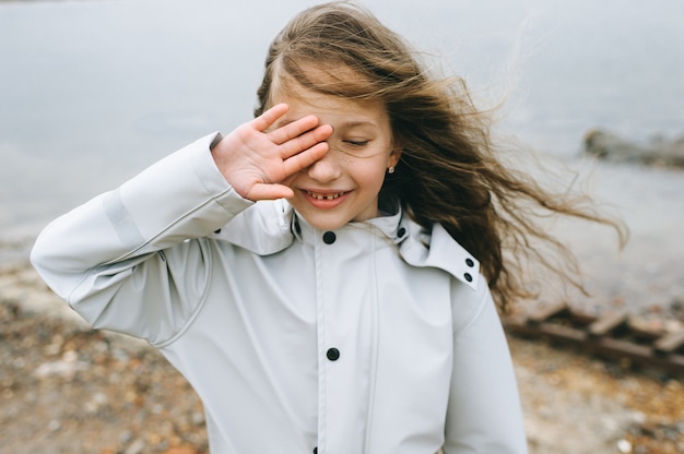 Retrato de una niña sonriente cerca del mar en el impermeable