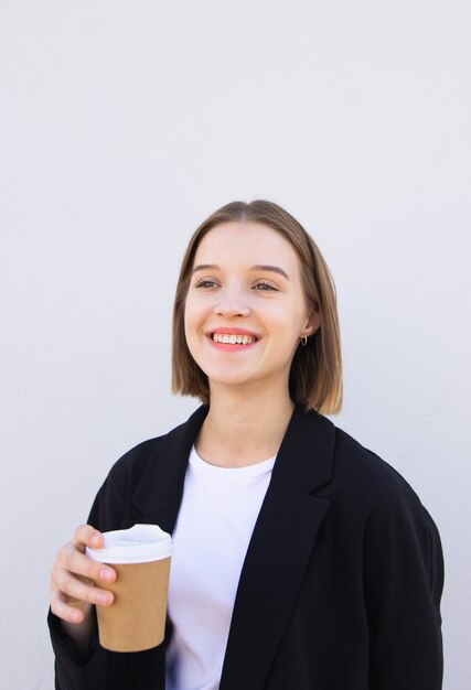 Retrato de una niña sonriente en una chaqueta con una taza de café en sus manos sobre blanco