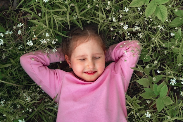 Retrato de una niña sonriente con coletas acostado en un prado de flores