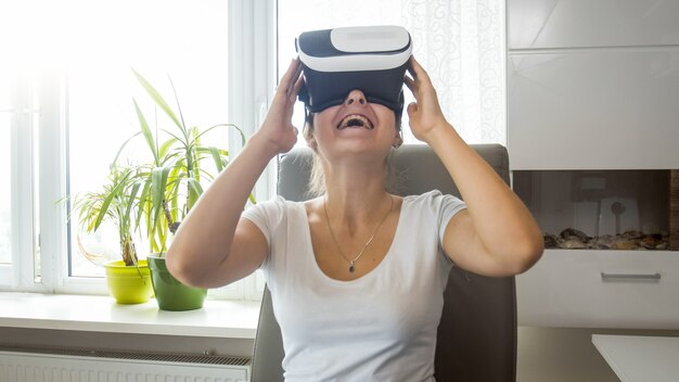 Retrato de niña sonriente emocionada sentada en casa y usando gafas de realidad virtual.