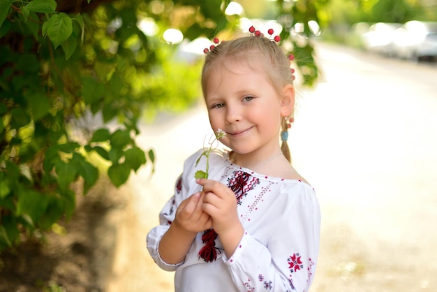 Retrato de una niña sonriente con una flor en una camisa bordada de Ucrania Kid girl huele una flor