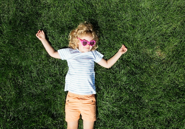 Retrato de una niña sonriente en gafas de sol en forma de corazón acostado