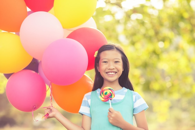 Foto retrato de niña sonriente con globos y chupetín en el parque