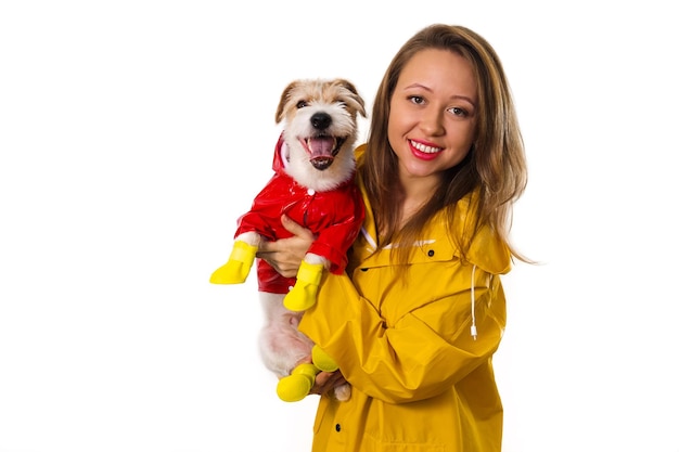 Retrato de una niña sonriente con un impermeable amarillo con un perro Jack Russell Terrier con una chaqueta roja en sus brazos. Aislado sobre fondo blanco