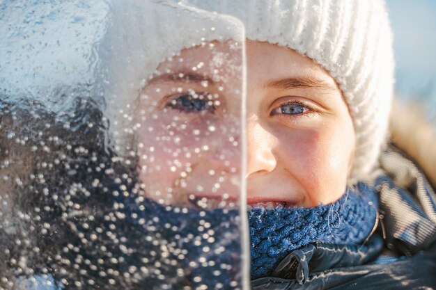 Retrato de niña sonriente mira a través de un trozo de hielo transparente en un día de invierno helado