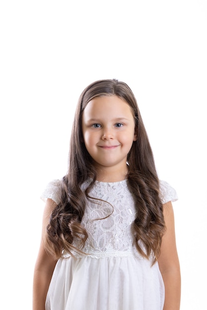 Retrato de niña sonriente modesta con rizos largos en vestido blanco aislado sobre fondo blanco con cop ...