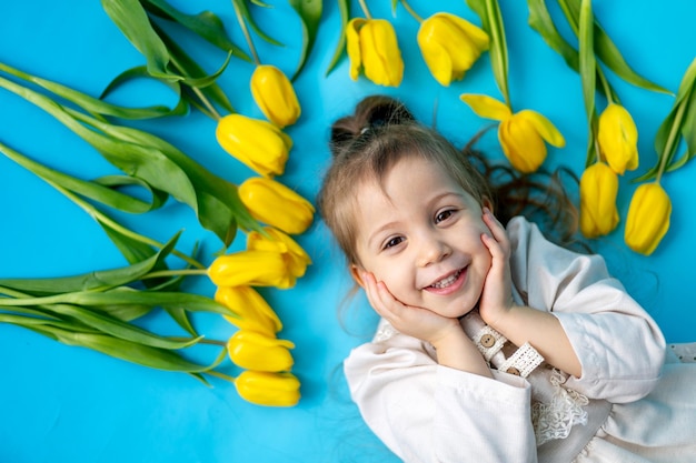 Retrato de una niña sonriente un niño con un ramo de tulipanes amarillos sobre un fondo azul aislado Estilo de vida Día Internacional de la Mujer o Día de la Madre Espacio para texto Fotografía de alta calidad