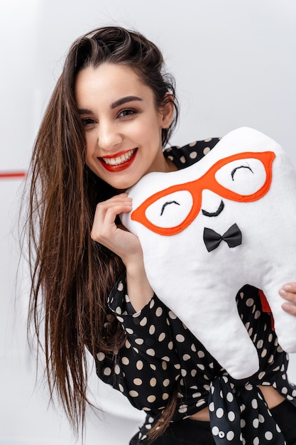 Retrato de una niña sonriente con peluche en las manos. Peluche con forma de diente.