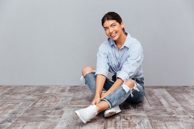 Retrato de una niña sonriente sentada en el suelo aislado en una pared gris