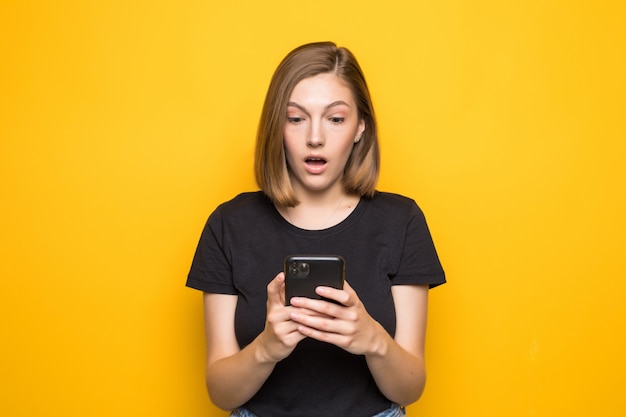 Retrato de una niña sonriente sosteniendo el teléfono móvil mientras está sentado aislado sobre la pared amarilla