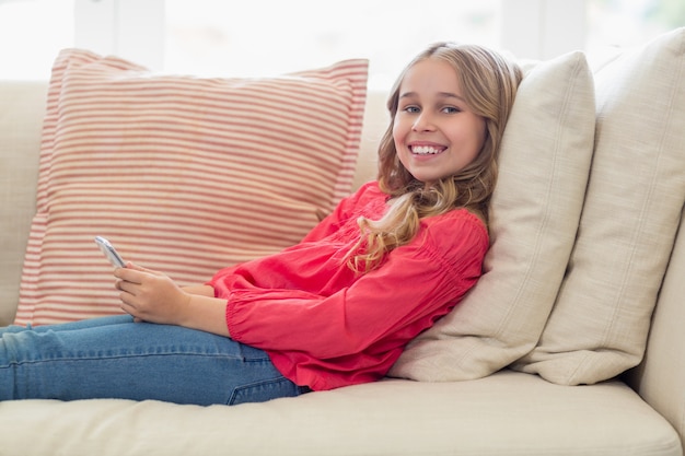 Retrato de niña sonriente con teléfono móvil tumbado en el sofá