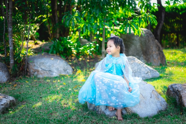 Retrato de niña sonriente en traje de princesa sentada en la roca en el parque