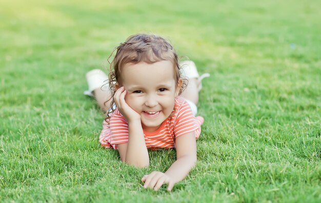 Retrato de una niña sonriente tumbado en la hierba verde.